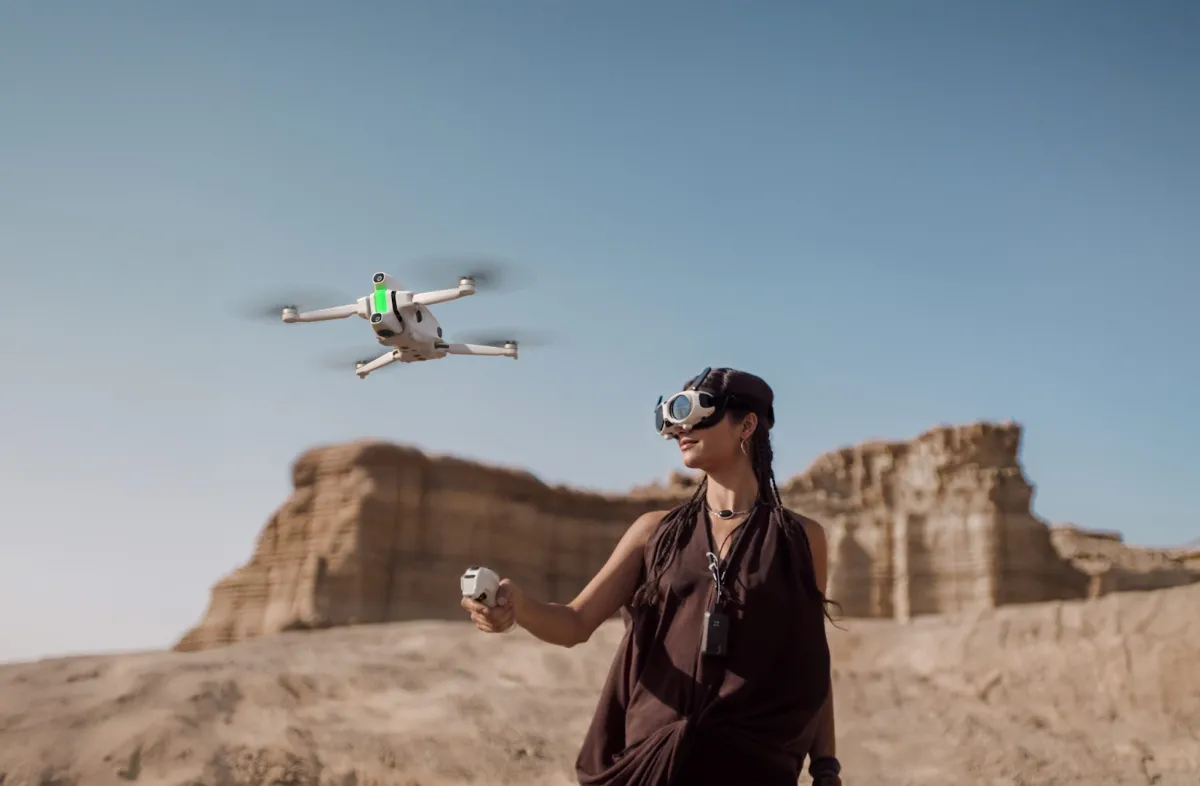 Woman wearing goggles flying the Insta360 Antigravity A1 drone with its hand controller in the desert